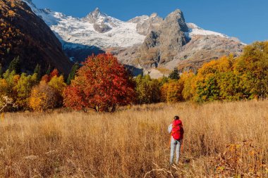 Sonbahar dağlarında sırt çantalı bir gezgin kadın. Buzul ve yürüyüşçü turistlerle dolu bir dağ.