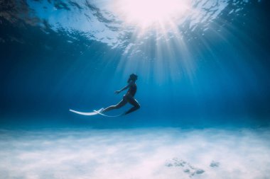 Beyaz yüzgeçli freediver süzülüyor ve güneş ışığıyla okyanusun altında poz veriyor..