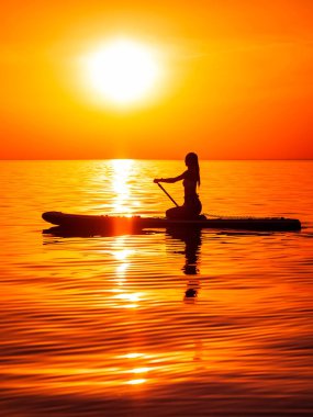 Sıska kız, sakin denizde günbatımında ya da gündoğumunda kürek çekiyor. Denizde kürek çeken bir kadın.