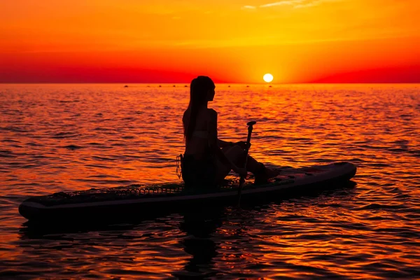 明るい夕日や日の出と静かな海でパドルボードに立つ女の子 女性は海でボード上でリラックス — ストック写真