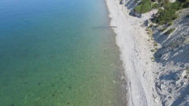 Sahil şeridinin sakin şeffaf denizi ve çam ağaçlı uçurumu. Denizde yaz günü