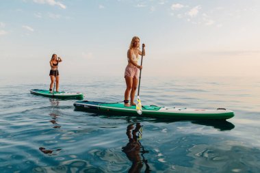 25 Haziran 2021. Anapa, Rusya. Sportif kızlar durgun denizde ayakta yüzer. Kadınlar Red Paddle SUP sörf tahtasında.