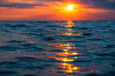 Bulutlu gün batımı, sıcak renkler ve okyanusta dalgalar.