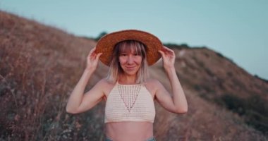 Hasır şapkalı neşeli kadın portresi mutlu bir şekilde kameraya bakıyor. Gün batımında açık havada başarılı bir hayat sürüyor.