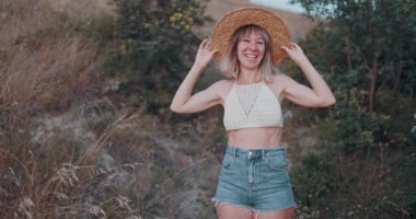 Hasır şapkalı genç bir kadının portresi. Gün batımında mutlu bir şekilde kameraya bakıyor ve yüzünü ekşitiyor.