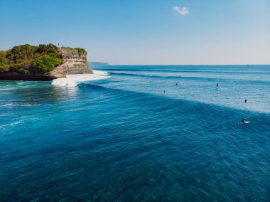 Mavi okyanusta uzun sörf dalgaları ve arka planda uçurum. Dalgalı tropik adanın havadan görünüşü