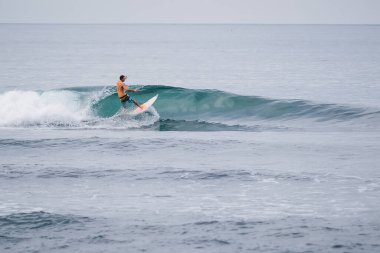 20 Ağustos 2021. Bali, Endonezya. Mavi dalgada sörf tahtasında sörfçü. Tropikal okyanusta sörf yapmak