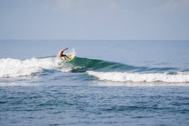 20 Ağustos 2021. Bali, Endonezya. Mavi dalgada sörf tahtasında sörfçü. Tropikal okyanusta sörf yapmak