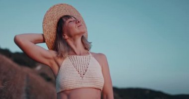 Hasır şapkalı kadın gün batımında dışarıda dinleniyor.