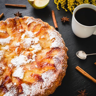 Siyah arka planda kahve fincanı ve tarçınlı Charlotte elmalı keki..