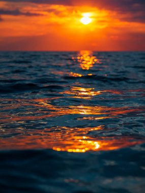 Bulutlu gün batımı, sıcak renkler ve denizde dalgalar.