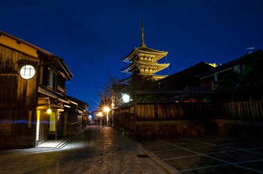 Kyoto 'da küçük bir caddede şehir manzarası. Alacakaranlıkta Yasaka Tapınağı' nı görebilirsiniz. Sokaklar turistlerin gölgesinde ve arabanın ışıkları uzun pozlardan bulanık..