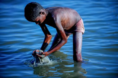 Varanasi / Hindistan - Mar 02 2013: Çocuk Ganga Nehri 'nde gömlek giymedi. Eğildi ve eliyle sudaki çöplerden değerli eşyalar aradı..