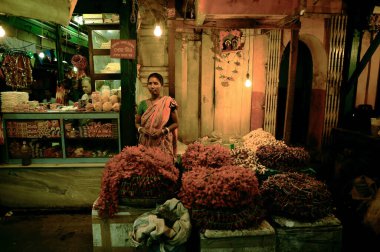 Varanasi / Hindistan - 02 Aralık 2013: Hintli kadın satıcı şehrin alacakaranlıkta bir çiçek standında duruyor, dramatik koyu tonlar.