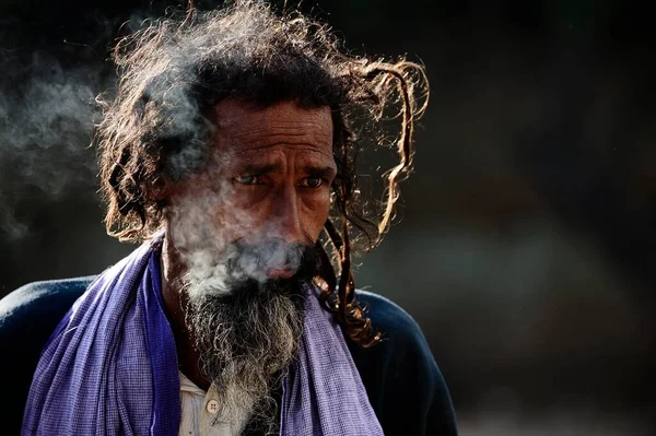 Varanasi India 2013年3月2日 一名亚洲男子 头发浓密 胡须蓬松 早上吸烟 创造出美丽的帽灯和烟雾 黑色背景上的暗色调 — 图库照片