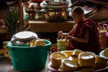 Üç Pagodas / Myanmar - 2016 Ağustos 29: Kırmızı bornoz giyen genç bir keşiş oturuyor ve kurabiyeyi temizliyor. Burma 'nın kırsal bir tapınağındaki mutfakta.