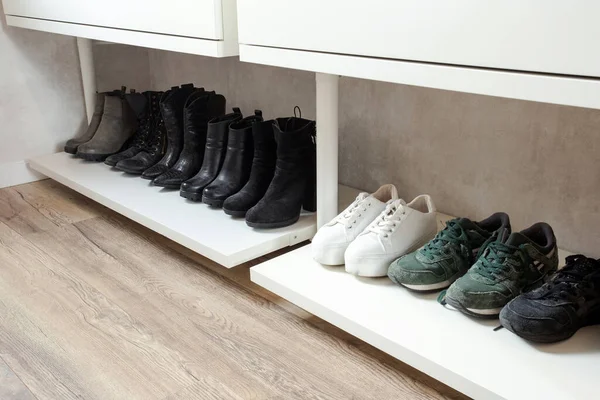Организованная обувная полка, обувная полка с черной стилистической обувью и сапогами, на деревянном полу, рядом с белой стеной. современный номер — стоковое фото