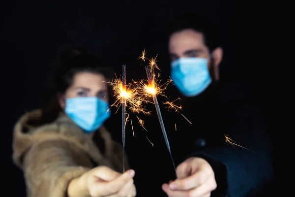 Pasangan muda mengenakan masker wajah pelindung untuk Coronavirus dan memegang kembang api selama malam tahun baru, 2021 dan konsep Covid-19 Stok Gambar