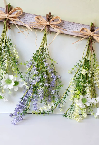 Various bright bouquet of dried flowers hanging on rope against wooden background, making dried flowers modern decoration for home interior