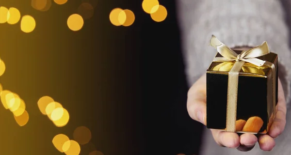 Рука держит золотую подарочную коробку с золотой лентой, боке блестящий фон, Рождество или День рождения подарок концепции с местом для текста — стоковое фото