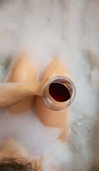 Jovens mulheres mão segurando copo de vinho na banheira, beber vinho tinto e deitado na banheira com espuma de bolha, vista superior, relaxamento e conceito de spa — Fotografia de Stock