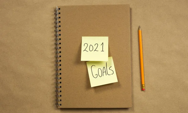 Cuaderno con notas amarillas adhesivas con 2021 y objetivos para Año Nuevo sobre fondo de papel marrón con lápiz clásico, negocio o escuela, concepto de educación. Copiar espacio — Foto de Stock