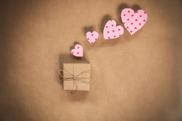 A romantic present wrapped in kraft paper with pink hearts for Valentines Day, plain brown eco friendly gift box, modern background design copy space top view