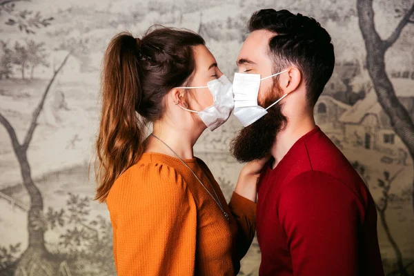 Giovane coppia romantica amorevole indossa una maschera protettiva per il coronavirus e baci, tenendo mazzo di fiori. Giorno di San Valentino e concetto Covid-19 — Foto Stock