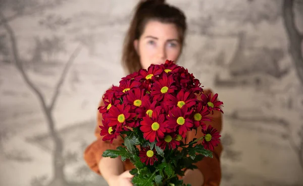 Gifts, celebration and tenderness concept. Surprised cute young female holding a bouquet of red flowers, daisies for Valentines Day or Birthday, romantic background