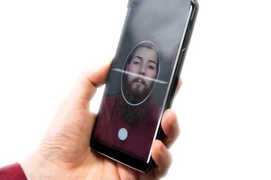 Cep telefonu tutan genç bir erkek, yüz değiştirme için selfie, derin sahte uygulama. Beyaz arkaplanda izole edilmiş diğer yüz taranıyor