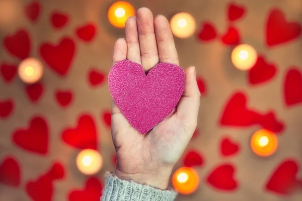 Main féminine tenant un coeur rose pailleté avec bougie romantique et fond de coeur rouge pour la Saint-Valentin ou concept romantique — Photo