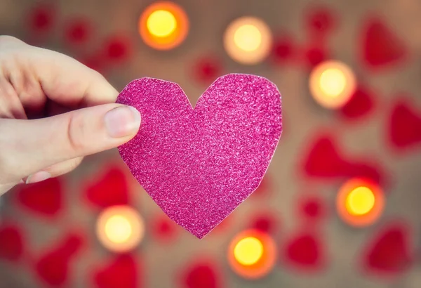Main féminine tenant un coeur rose pailleté avec bougie romantique et fond de coeur rouge pour la Saint-Valentin ou concept romantique — Photo