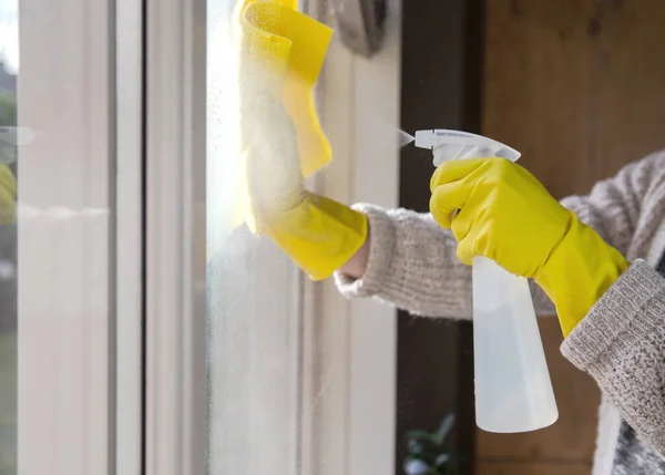 Limpieza de una ventana con detergente en aerosol, guantes de goma amarilla y paño de cocina en el concepto de superficie de trabajo para la higiene, el negocio y el concepto de salud — Foto de Stock