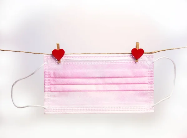 Różowa ochronna maska medyczna wisząca z kołki odzieżowe w kształcie serca izolowane na białym tle, Zdrowie, Covid-19 lub Walentynki koncepcja tła — Zdjęcie stockowe