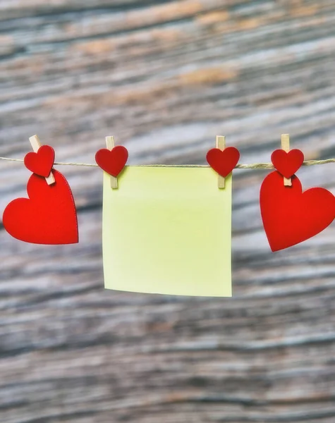 Nota adhesiva en blanco con corazones rojos colgando sobre fondo de madera, Día de San Valentín, Concepto de Día de las Madres para Mujeres, Espacio para copiar — Foto de Stock