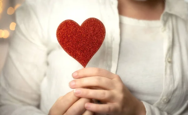 Mani femminili che tengono il cuore rosso scintillante vicino al corpo, prendendosi cura, Salute, concetto di San Valentino design romantico — Foto Stock