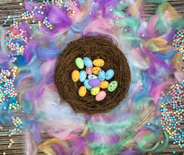 Colorful Easter eggs in bird nest surrounded with pastel colored feathers and wooden cubes with the text Happy Easter top view, modern background design, Easter holliday, Spring, concept — Stock fotografie