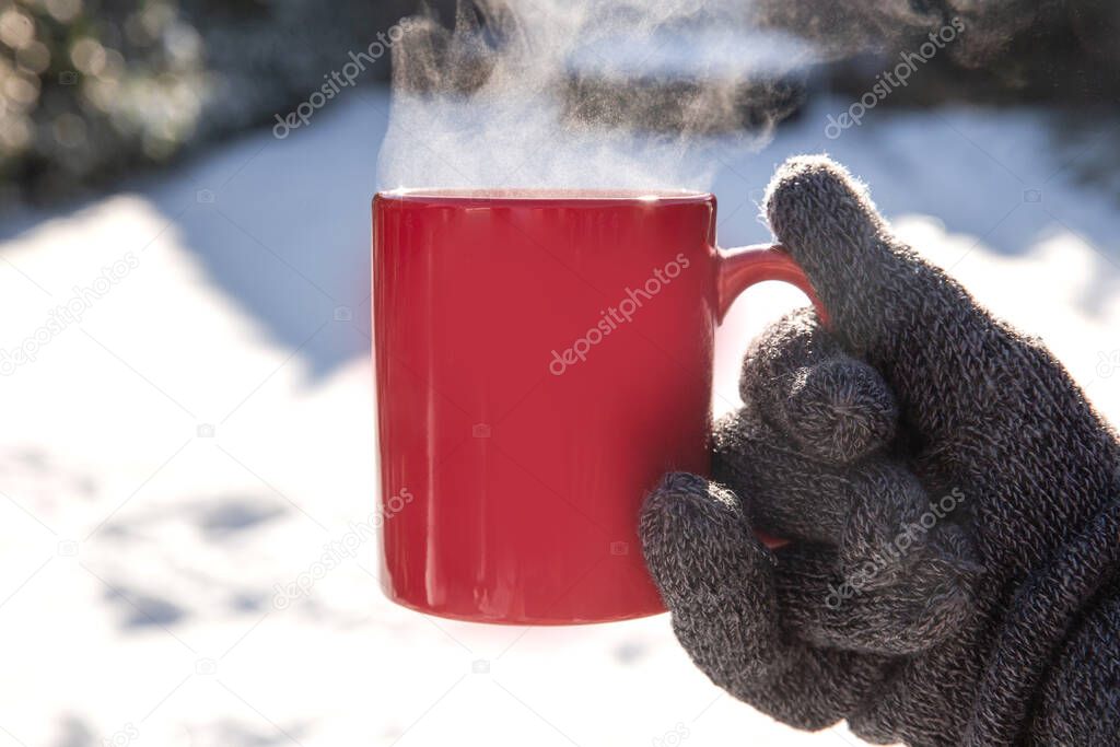 Person holding a red mug with hot coffee,tea or Chocolate milk with steaming smoke and gloves in the snow, Winter,relaxtion,drink,snow,cozy concept background