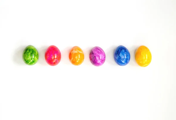 Fila de ovos de Páscoa pintados coloridos isolados no fundo branco rodeado de flores vista superior fundo, conceito feliz Páscoa design moderno — Fotografia de Stock