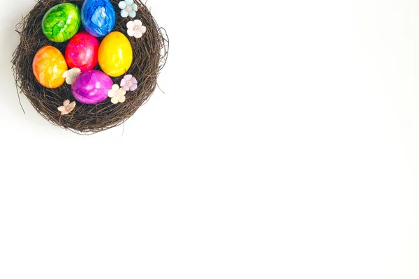Barevné malované ručně vyrobené velikonoční vajíčka v hnědém hnízdě izolované na bílém pozadí horní pohled, Veselé Velikonoce dovolená koncept, s krásnými jarními květy — Stock fotografie