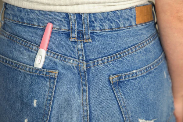 Young woman with positive pregnancy test in pocket of jeans close-up motherhood happiness modern retro background