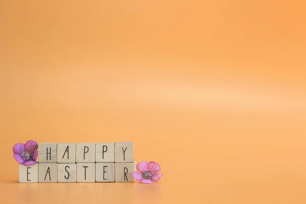Текст поздравления с праздником Пасхи на ярко-оранжевом пастельном фоне с фиолетовыми весенними цветами, концепция поздравительной открытки, весна, Пасха с копировальным местом — стоковое фото
