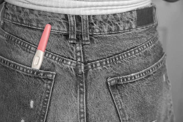Young woman with positive pregnancy test in pocket of jeans close-up black and white