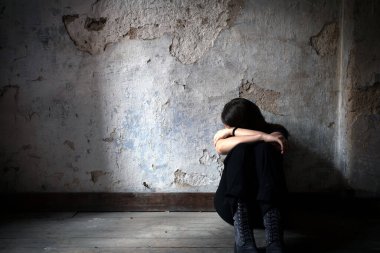 Depresyonda ve yalnız bir kız, terk edilmiş pis bir odada yalnız başına oturuyor. Ahşap zeminde. Mutsuz ve endişeli bir şekilde hayatı, depresyonu ve bağımlılık sorunları üzerine ağlıyor.