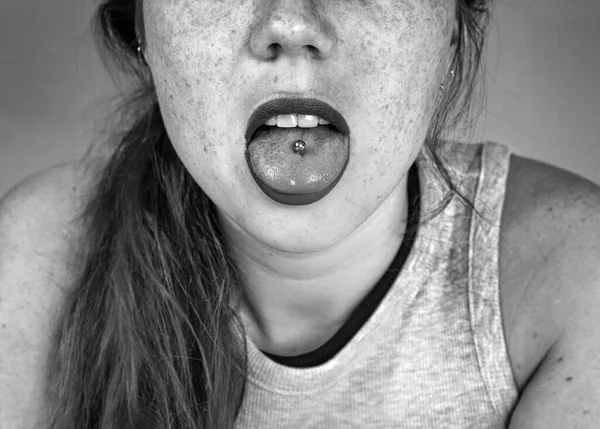 Close-up portret van jonge vrouw steken uit pierced tong, tonen haar tong piercing zwart-wit — Stockfoto