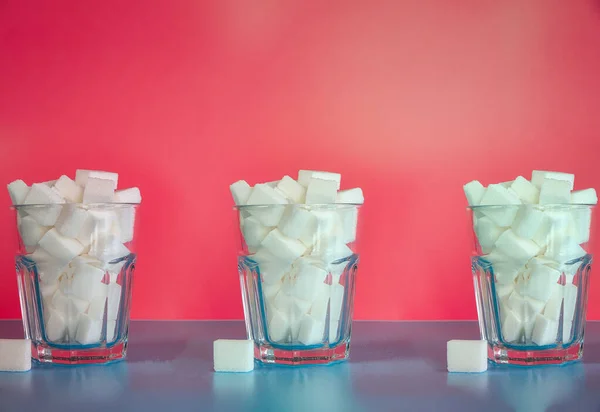 Trzy szklanki pełne kostek cukru na różowym tle, cukier, niezdrowe, słodycze, koncepcja żywności śmieci tło retro nowoczesny design — Zdjęcie stockowe