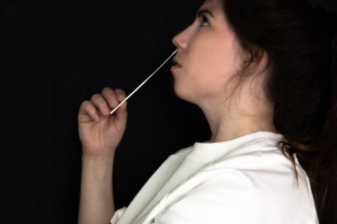 Corona salgını sırasında siyah arka plan üzerinde Covid-19 SARS-CoV-2 testi yaptıran genç bir kadın, hızlı ev testi Coronavirüs