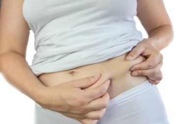 Beyaz iç çamaşırı giyen genç bir kadın göbek yağlarını kontrol ediyor ve sıkıyor. Sağlıklı yaşam tarzı beyaz arka planda izole edilmiş.