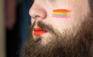 Yanağında gurur bayrağı olan genç, sakallı yakışıklı bir adam, gökkuşağı bayrağı LGBTQ, cinsiyet hakkı ve cinsel azınlığı temsil ediyor. Portre