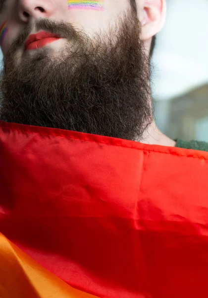 Young handsome bearded man with pride flag on his cheek, rainbow flag standing for LGBTQ, Gender right and sexual minority. Portrait — Stock Photo, Image